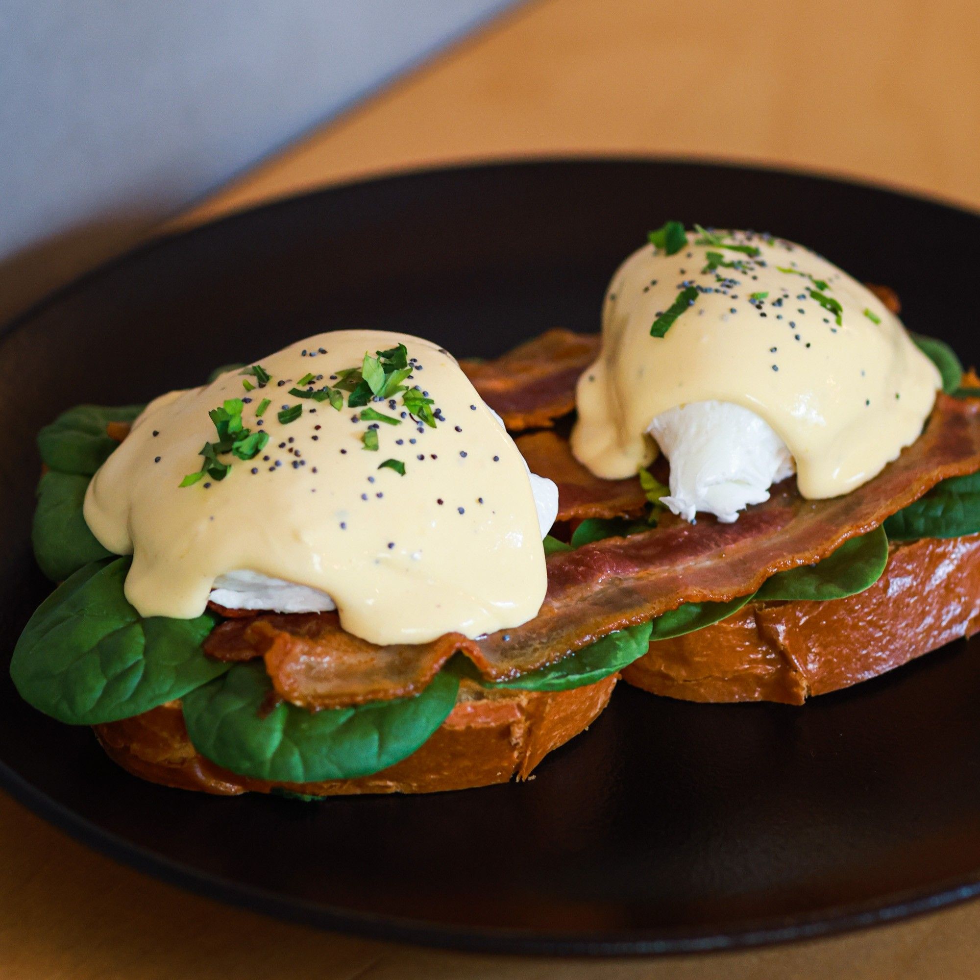 Eggs Benedict with crispy bacon, spinach, hollandaise and poppy seeds on toasted brioche