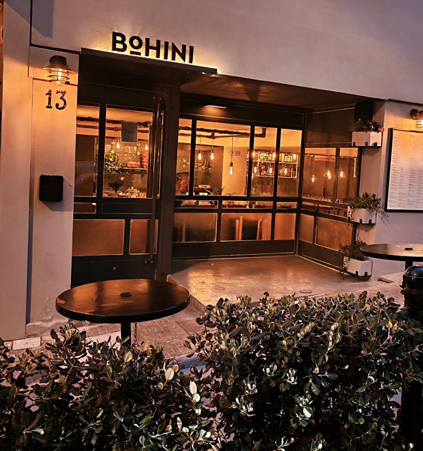 The front of Bohini at dusk: the lit BOHINI sign above number 13, warm lights through the windows and outdoor tables