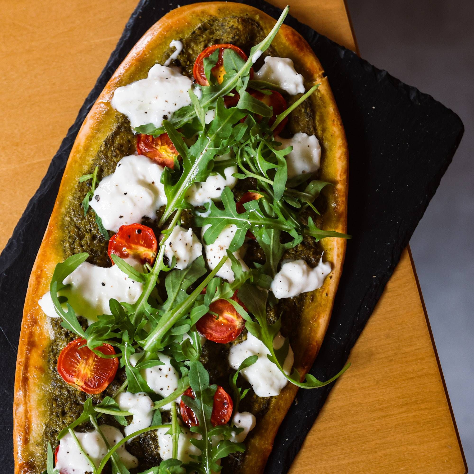 Basil pesto flatbread with roasted cherry tomatoes, rucola and burrata on a slate board